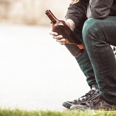 Man depressed with wine bottle sitting on bench outdoor