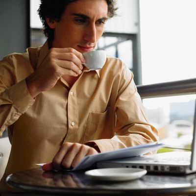Young businessman using laptop sitting at table drinking coffee