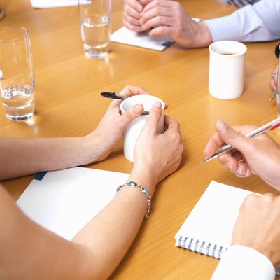 Business colleagues with drinks and notepads on table in meeting