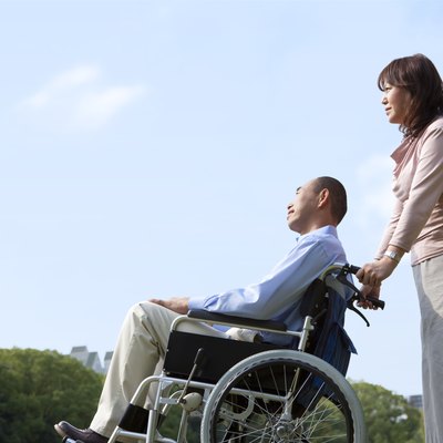 Mature couple in park, woman pushing man in wheelchair, copy space