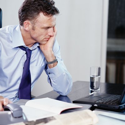 Businessman using laptop at desk, resting hand on phone