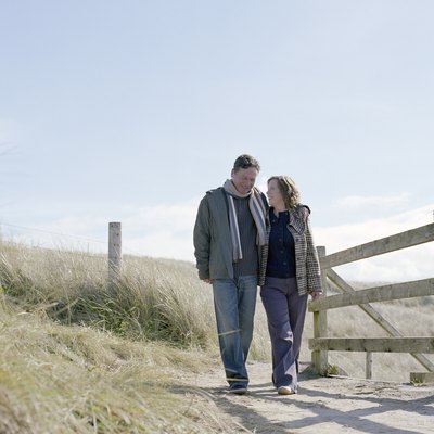 Mature couple walking on path by wooden rail, smiling