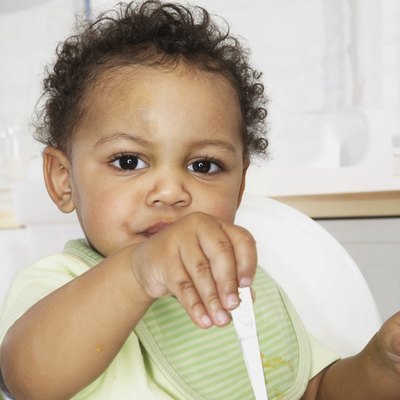 Baby boy (18-24 months) in high chair holding spoon in bowl, portrait