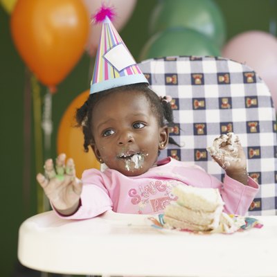 African baby in high chair wearing party hat and eating cake