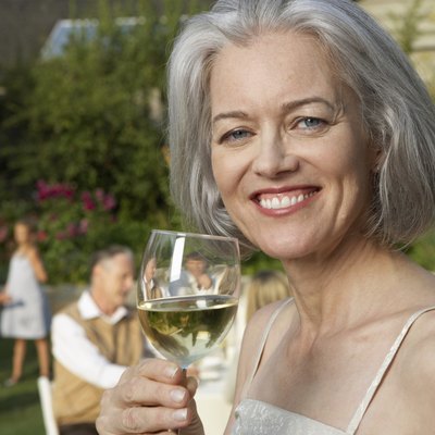 Mature woman in garden holding wine glass, smiling, portrait, close-up