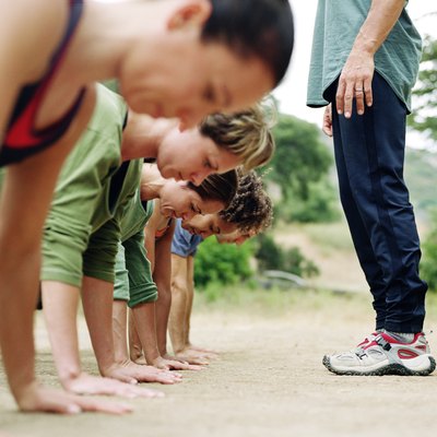 Man standing over group of people doing pushups, side view