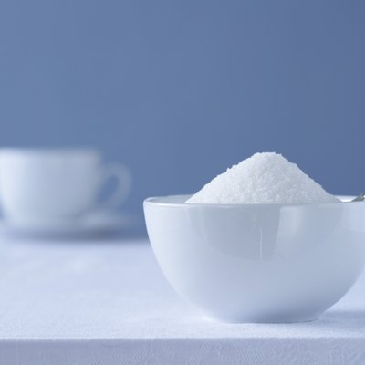 Bowl of sugar on table, tea cup in background