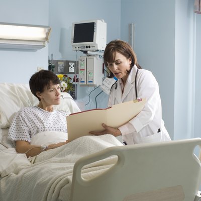 Female doctor showing medical chart to female patient lying in hospital bed