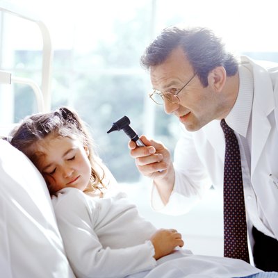 portrait of a male doctor examining a young girls ears with a otoscope