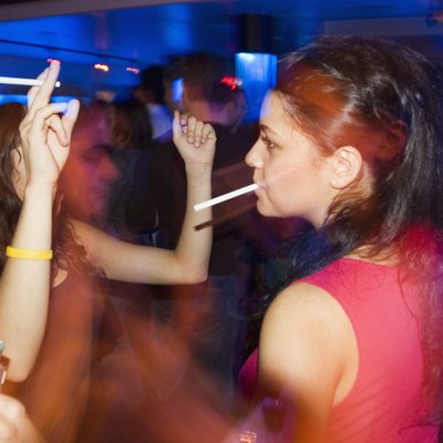 Close-up of two women smoking and dancing in nightclub, with people in the background
