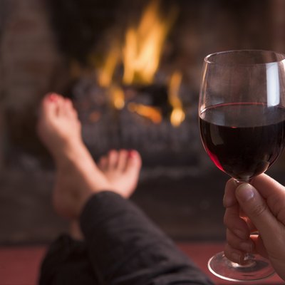 Feet warming at fireplace with hand holding wine