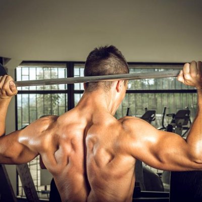 Young teenage man doing weighnt lifting with barbell. View from back.