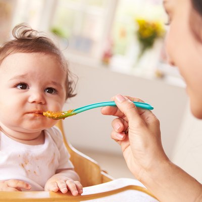 Happy Baby Being Fed In High Chair At Meal Time