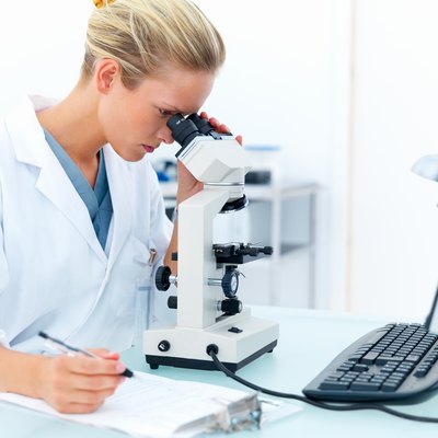 Female researcher looking into a microscope and writing notes
