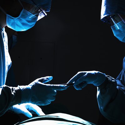 Two surgeons working and passing surgical equipment in the operating room, dark