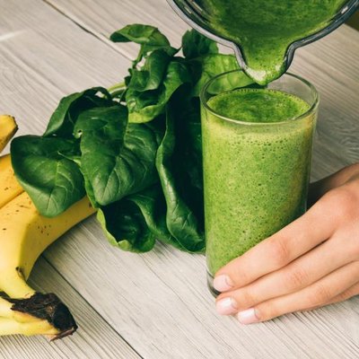 Female hand pours a smoothie of banana and spinach in glass on a wooden background