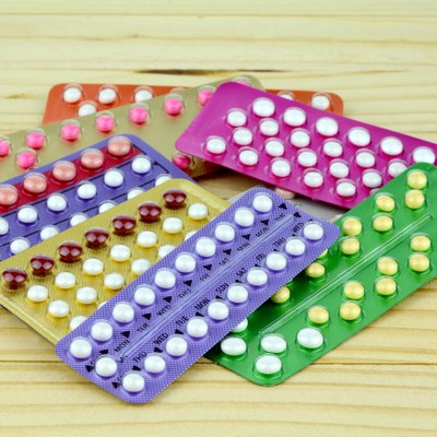 Colorful oral contraceptive pill strips on pine wood table.