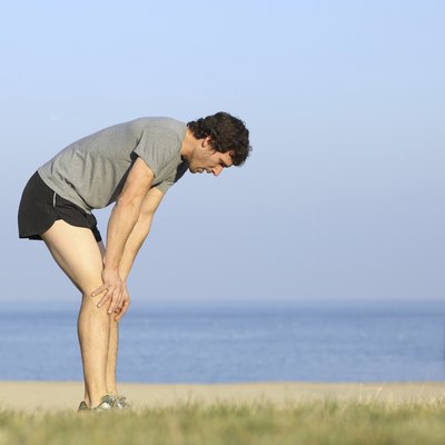 Exhausted runner man resting on the beach after workout