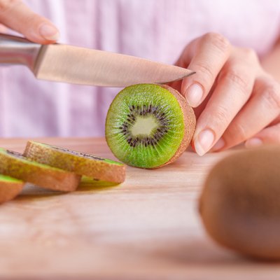 Woman food preparation - cutting a kiwi fruit.
