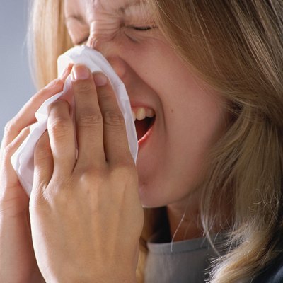 Woman sneezing, holding tissue to nose