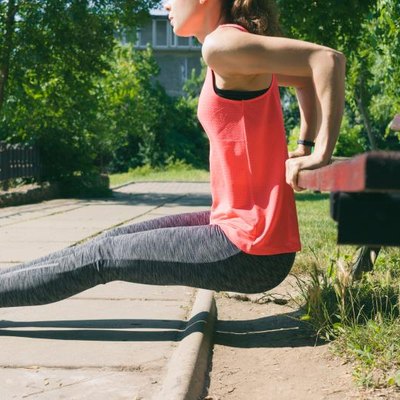 Woman in sportswear doing exercise on triceps on a park bench