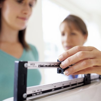 Doctor adjusting balance on weighing scale while patient checking weight