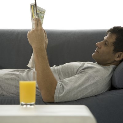 Mature man lying on couch and reading newspaper