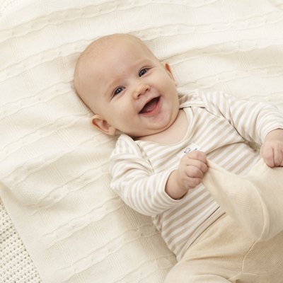Baby girl (3-6 months) lying on blanket, smiling