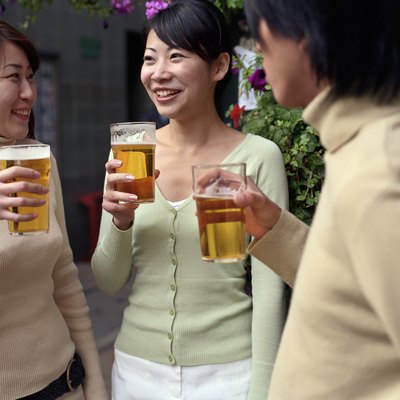 Two young women and young man holding pints of beer outside pub