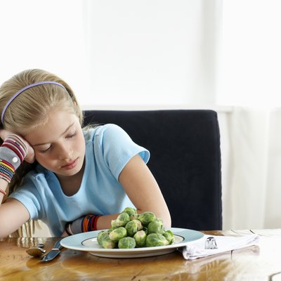 Girl (9-11) sitting at plate of sprouts