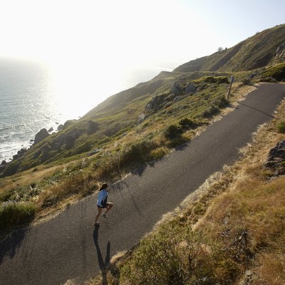 Woman jogging on road beside ocean, California, USA