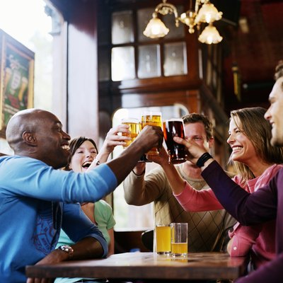 Group of friends around pub table, toasting drinks, smiling, side view