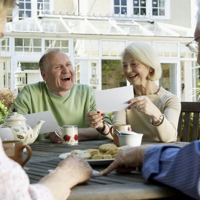 Two senior couples looking at photographs around garden table, smiling
