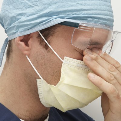 Male doctor wearing surgical mask and cap, rubbing eyes, side view
