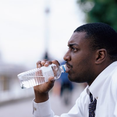 Side profile of a young man drinking water from a bottle outdoors