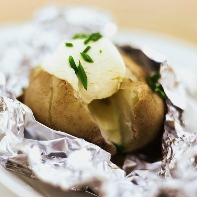 close-up of baked potato served with sour cream in foil