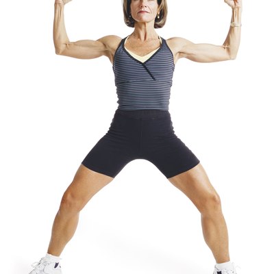 an adult caucasian woman is wearing black and gray as she stands with legs apart and arms up showing her muscles