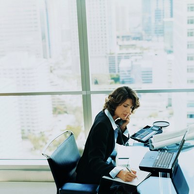 Businesswoman Sitting at Her Desk Using the Phone and Writing in a Notepad
