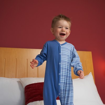 Smiling toddler boy standing atop hotel bed