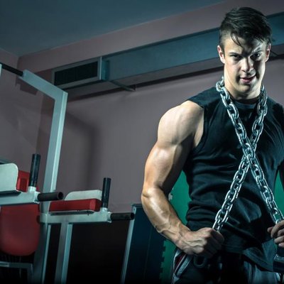 Young adult man posing in gym wearing iron chain around neck.