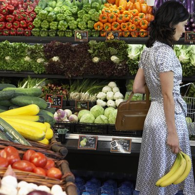 Woman holding bananas in produce aisle of supermarket, side view