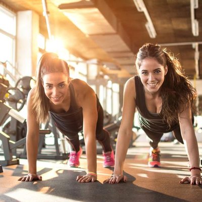 Two sporty girls doing push ups in gym.