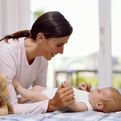 Mother holding baby girl's (6-9 months) legs, smiling