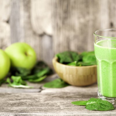 green smoothie juice on wooden table with spinach and apples