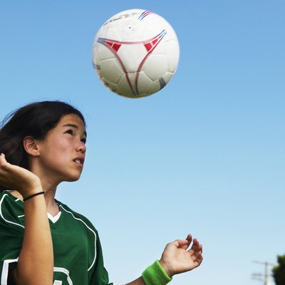 Female footballer (11-13) heading ball, low angle view