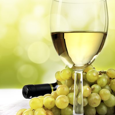 White wine glass, grapes and bottle on table in vineyard