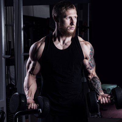 athletic guy bodybuilder , execute exercise with dumbbells, in dark gym