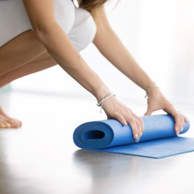 Close up shot of female hands unrolling yoga mat in a modern apartment, preparing for practice in class or at home. Yoga studio etiquette. Healthy lifestyle concept