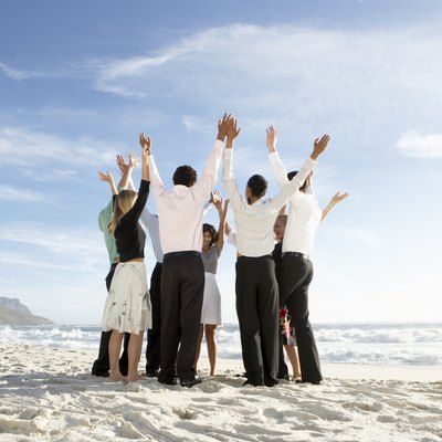 Group of people standing in circle on beach, arms raised