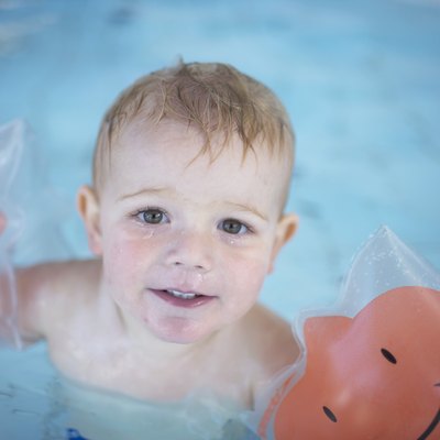 Boy (18-21 months) wearing armbands in swimming pool, portrait